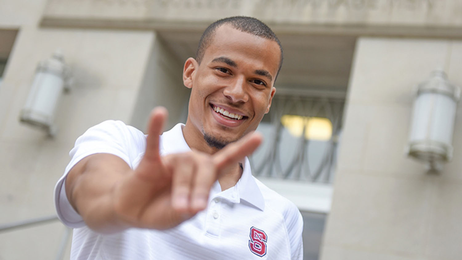 An NC State employee smiles while making the Wolf Ears gesture with their left hand.