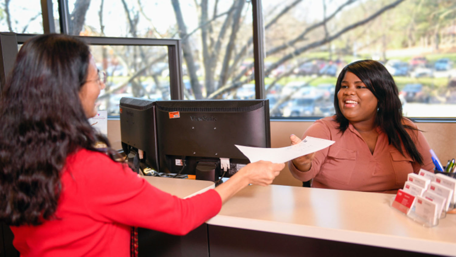 Two people in an office, one of them is handing a piece of paper over a counter to someone else.