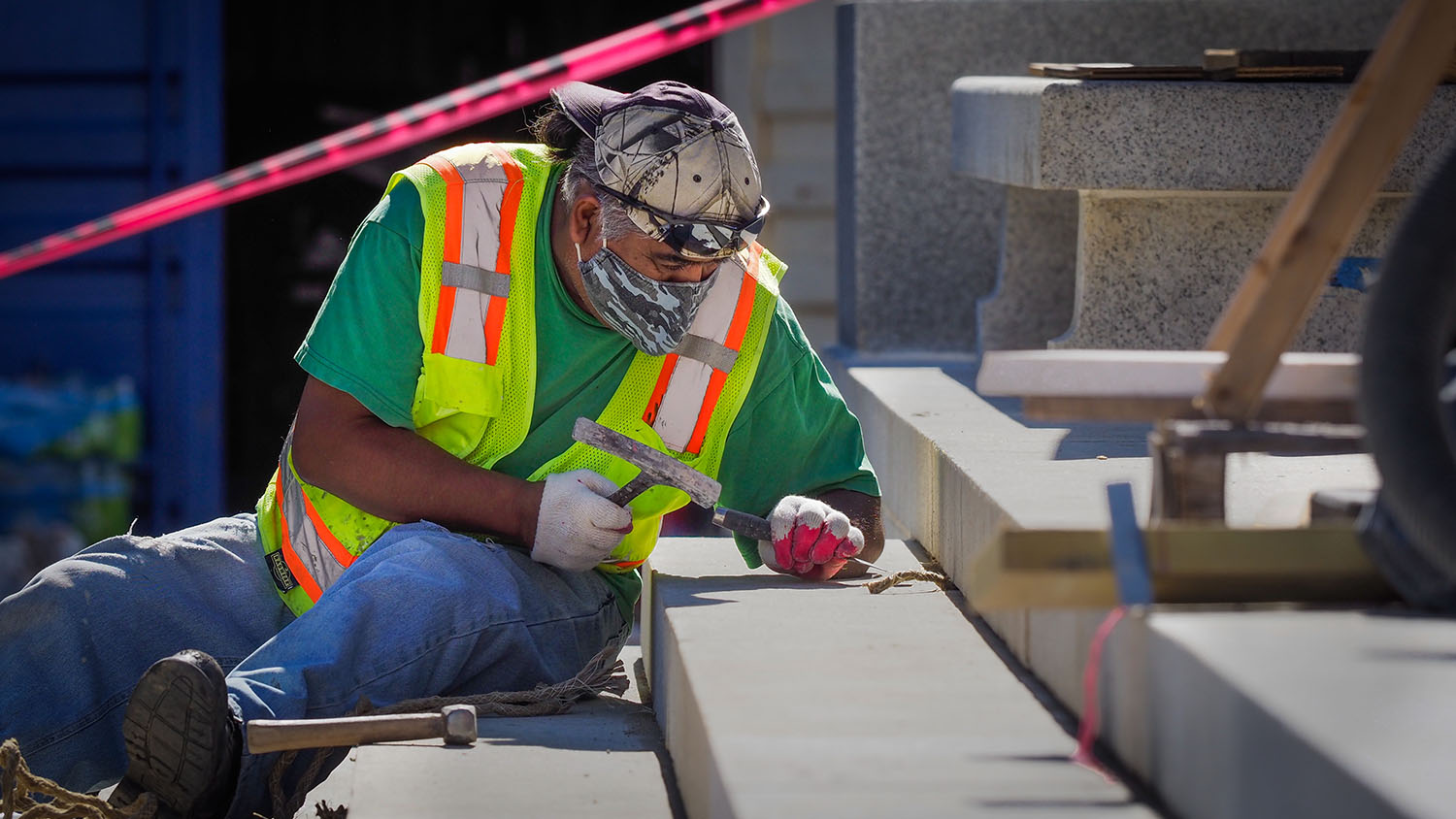 A Facilities employee conducts maintenance work on a stone stairway with hammer and chisel.