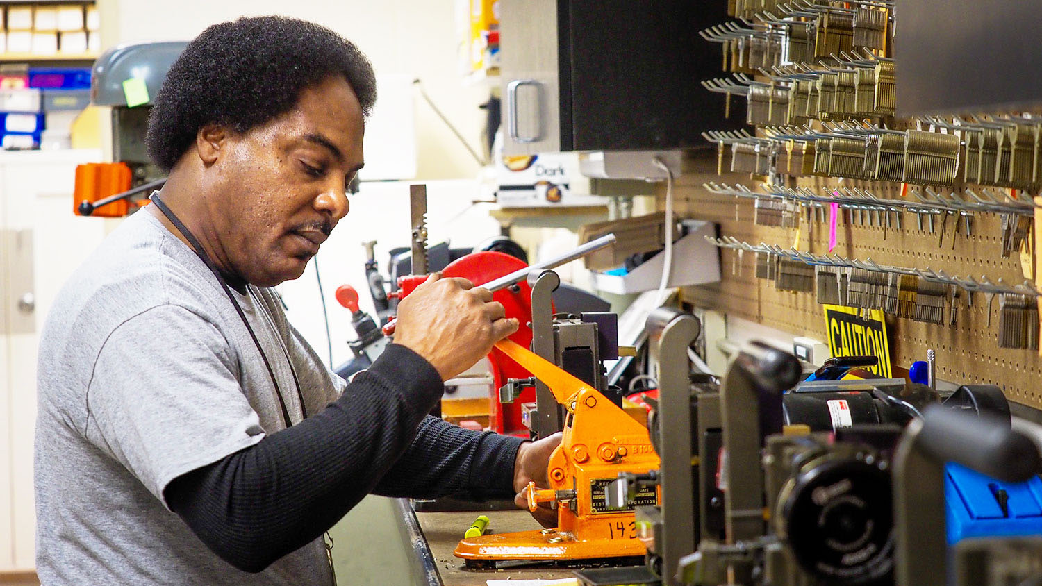 A locksmith works with a key cutting machine in a shop environment.