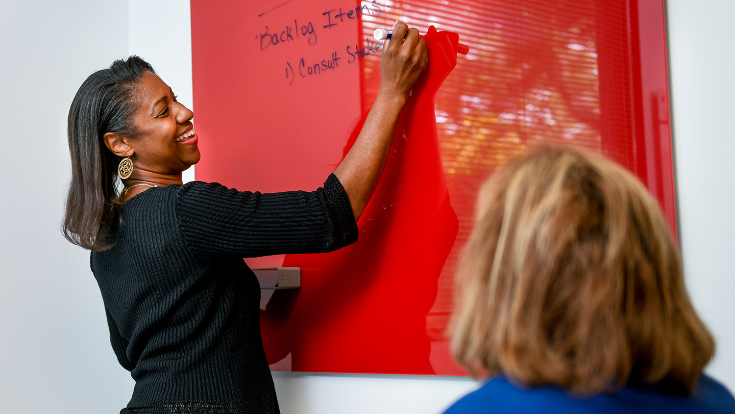 a person writes notes on a red dry erase board